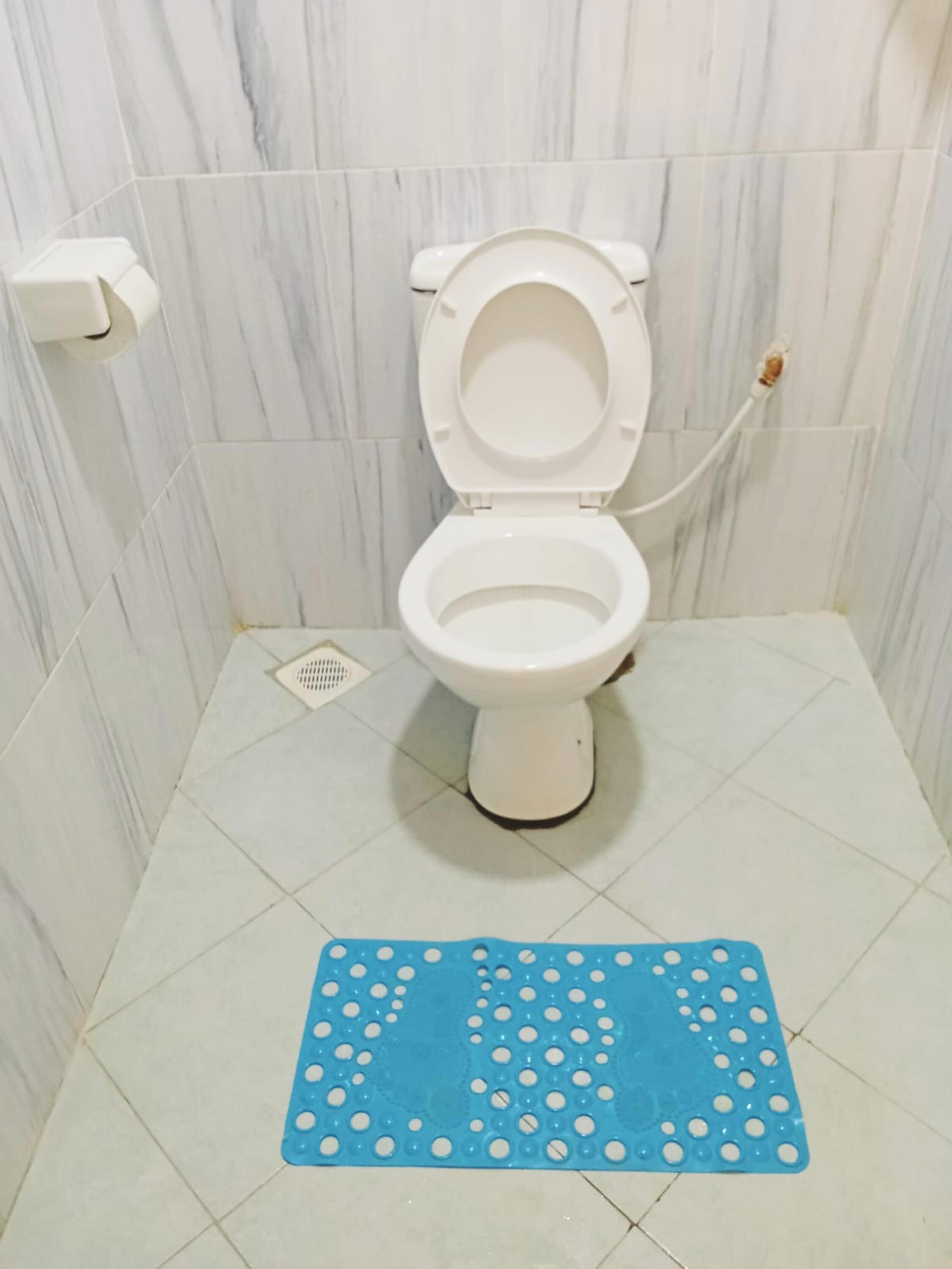 A bathroom with a white toilet, marble walls, and a blue mat with white dots.