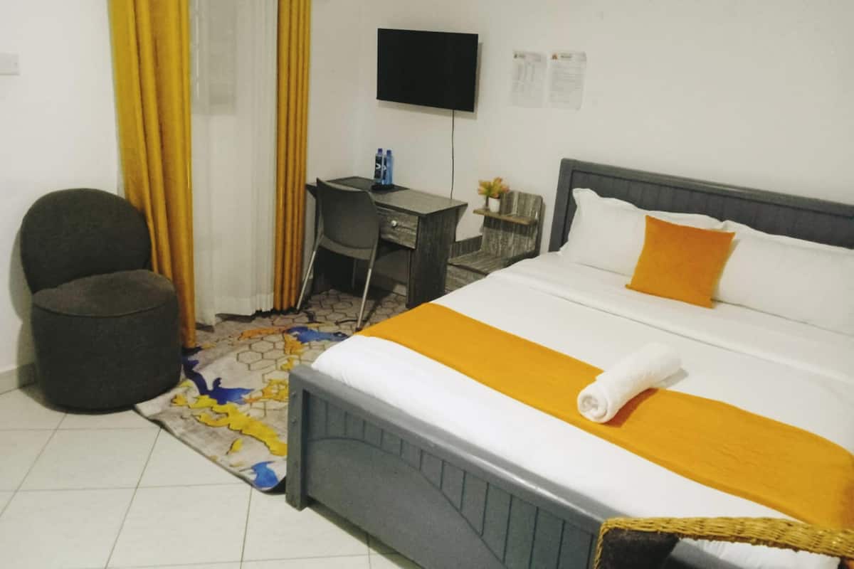 A hotel room with a bed, a desk, a chair, a television, and a small table with a plant.