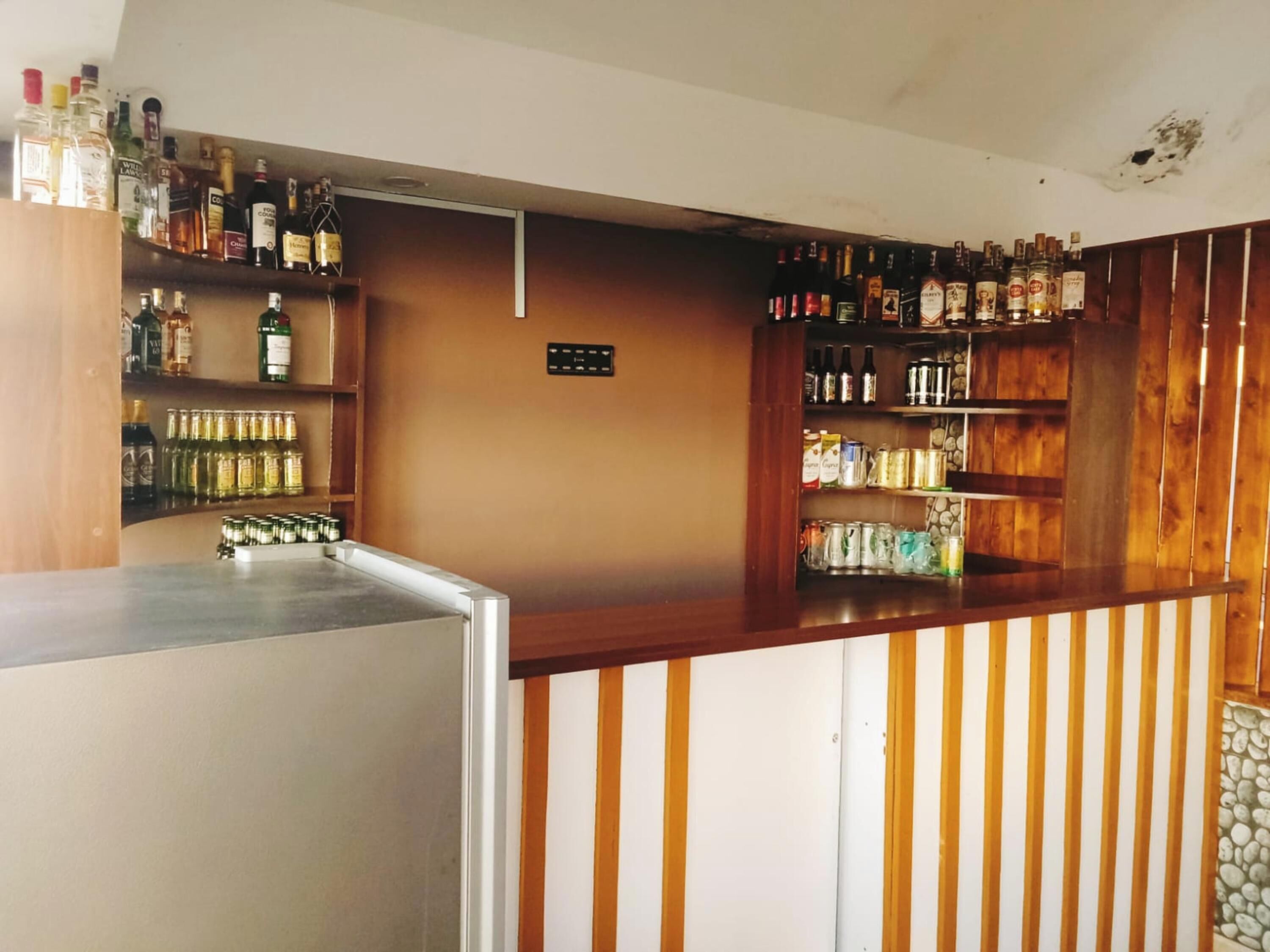 Eine Bar mit Regalen voller Spirituosenflaschen, einer Kasse und einer Holztresen.