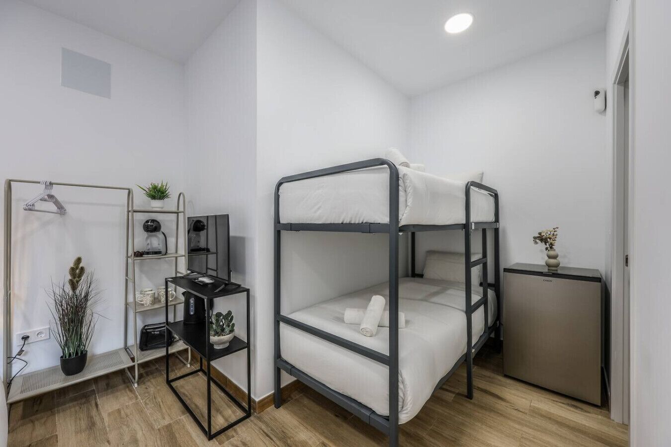 A compact room with a bunk bed, a desk with a chair, a small cabinet, and a potted plant.