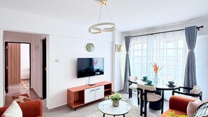 Una sala de estar moderna con sofá, televisor, mesa de comedor y vistas a la ciudad.