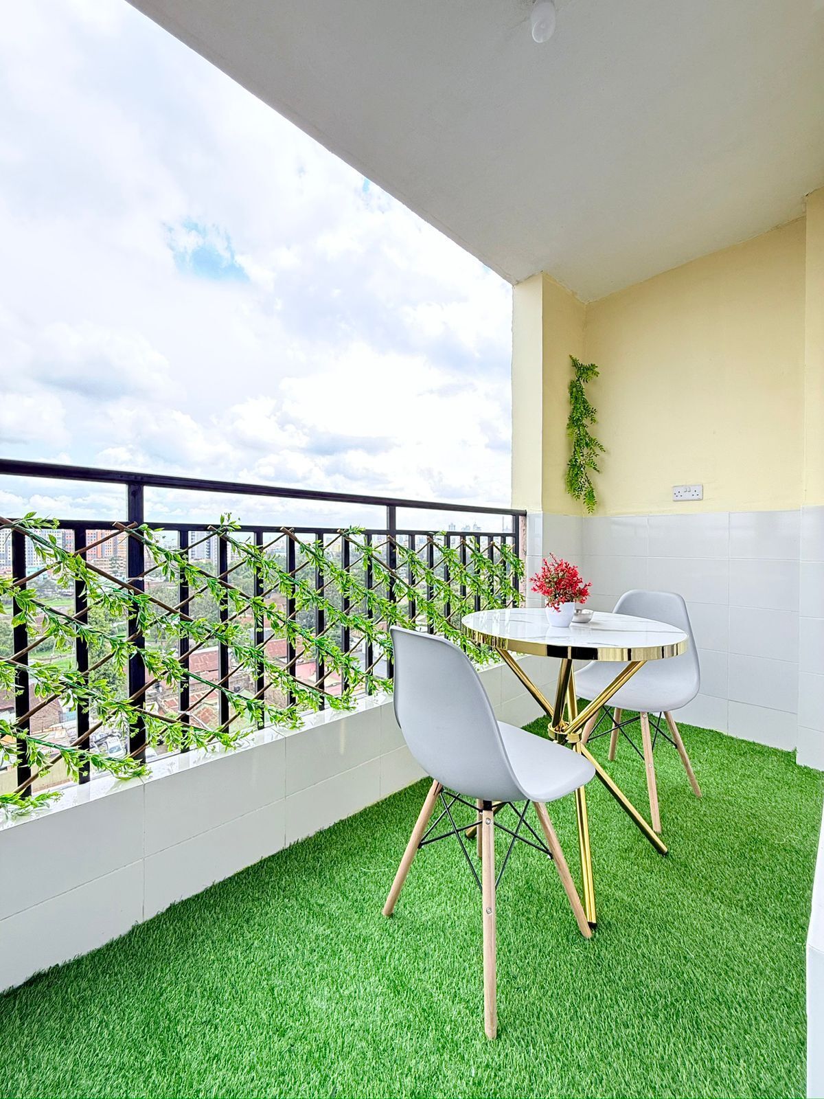 A balcony with artificial grass, a table with two chairs, and a view of the cityscape.