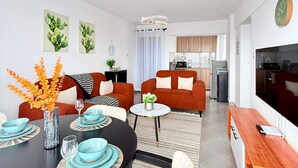 Una sala de estar moderna con comedor, una cocina al fondo y un televisor montado en la pared.