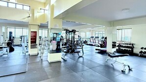 Un gimnasio amplio con diversos equipos de ejercicio, ventanas grandes y un techo alto.
