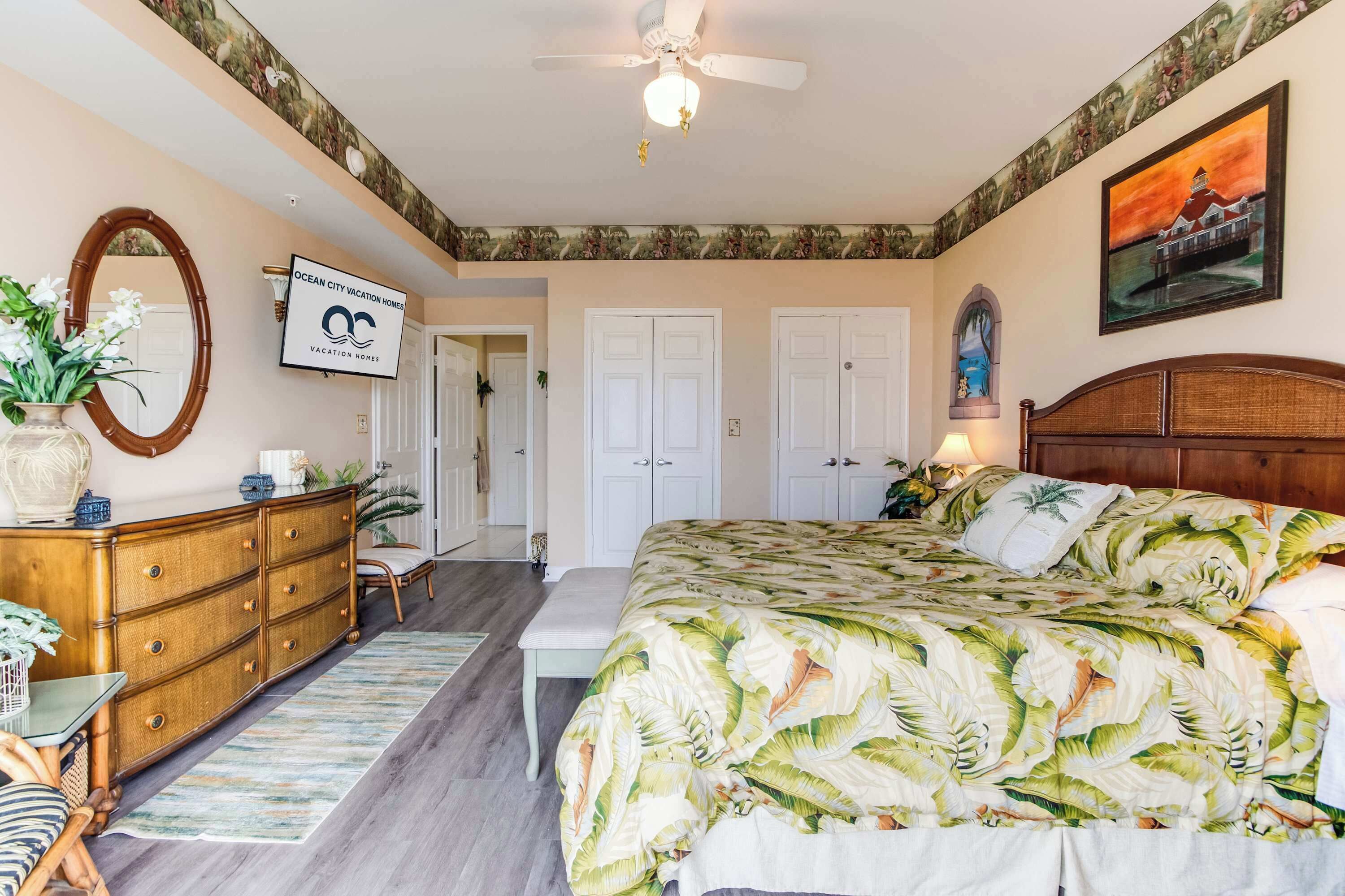 Une chambre à coucher avec un lit, une commode, un miroir, un ventilateur de plafond et un tableau accroché au mur.