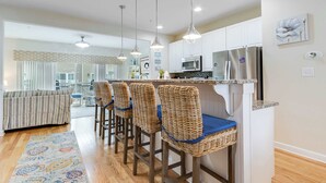 A modern kitchen with white cabinets, stainless steel appliances, and a bar area with wicker stools. - Broadmarsh 115C (Ocean City)