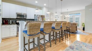 A kitchen with white cabinets, a microwave, a coffee maker, and wicker bar stools with blue cushions. - Broadmarsh 115C (Ocean City)