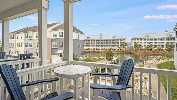 A covered outdoor area with a table and chairs, a view of a lake, and buildings in the background. - Broadmarsh 115C (Ocean City)