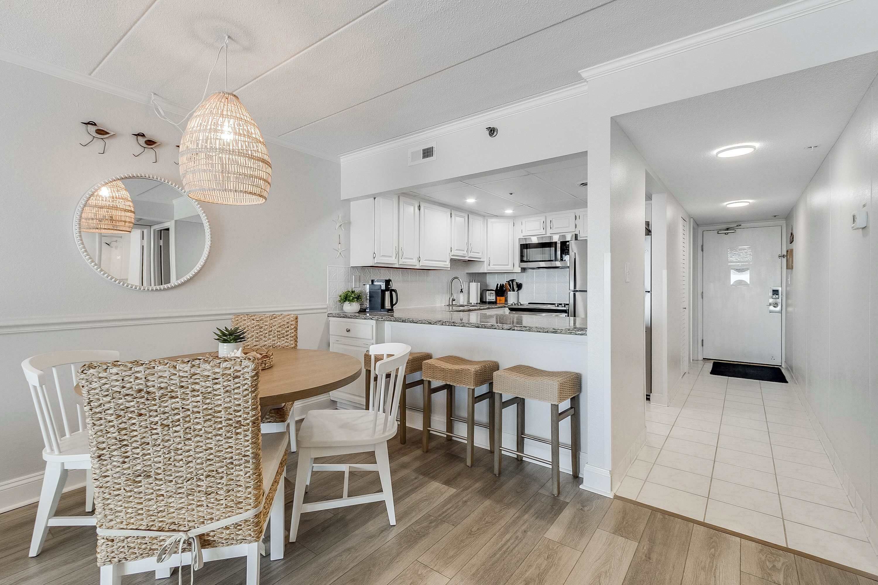 A modern kitchen with white cabinets, a round mirror, and a hanging light fixture.