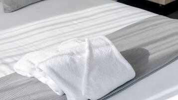 Ein ordentlich bezogenes Bett mit einer grau-weißen Streifenauflage, einem weißen Kopfkissen und einem weißen Handtuch.
