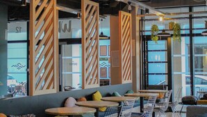 Un espacio interior moderno con zonas de estar, mesas y plantas colgantes.
