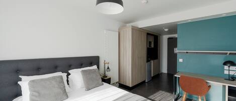 Ein modernes Hotelzimmer mit Bett, Schreibtisch, Stuhl und einer Küchenzeile.