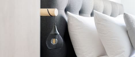 Un dormitorio moderno con un cabecero capitonado, una mesita de noche negra, una lámpara y ropa de cama blanca.