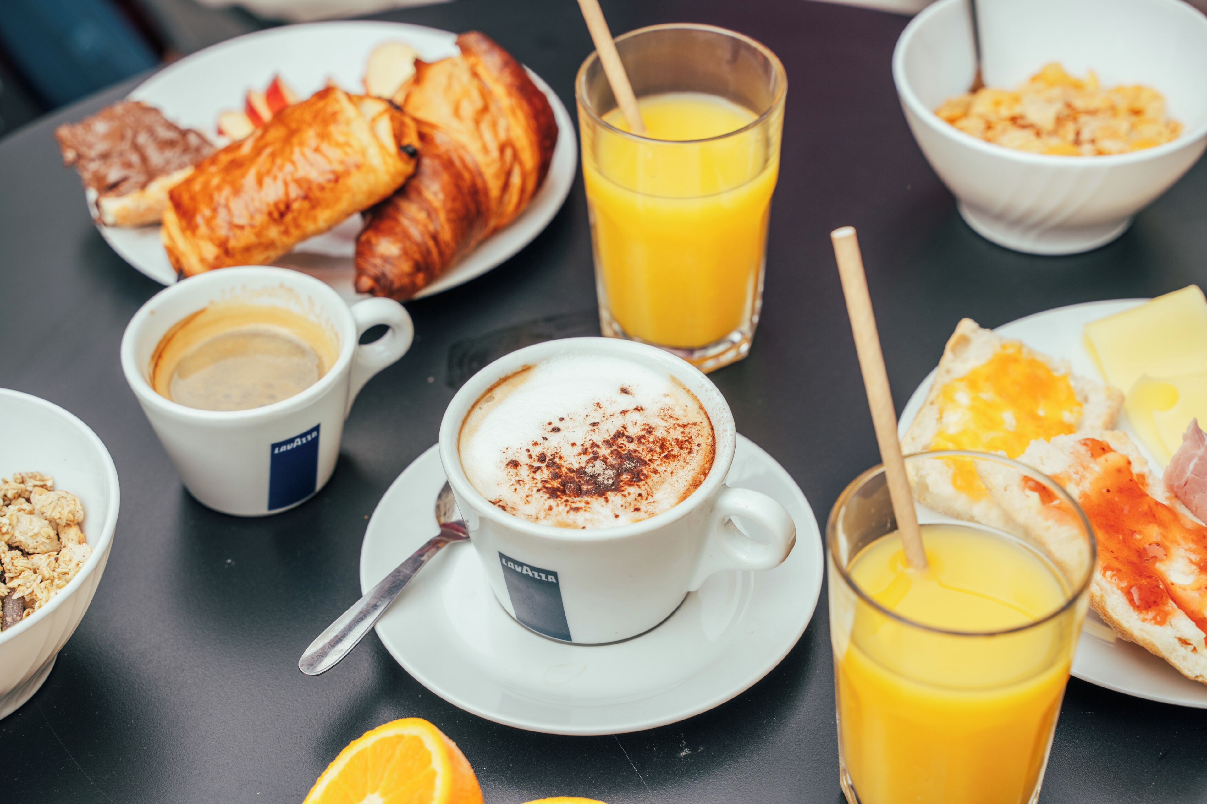 Ein Frühstückstisch mit Croissants, einer Kaffeetasse, einem Glas Orangensaft und einer Schüssel Müsli.