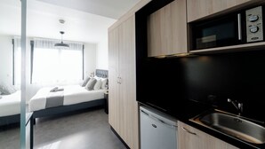 Una habitación de hotel moderna con cama, una kitchenette pequeña y ventana con cortinas.