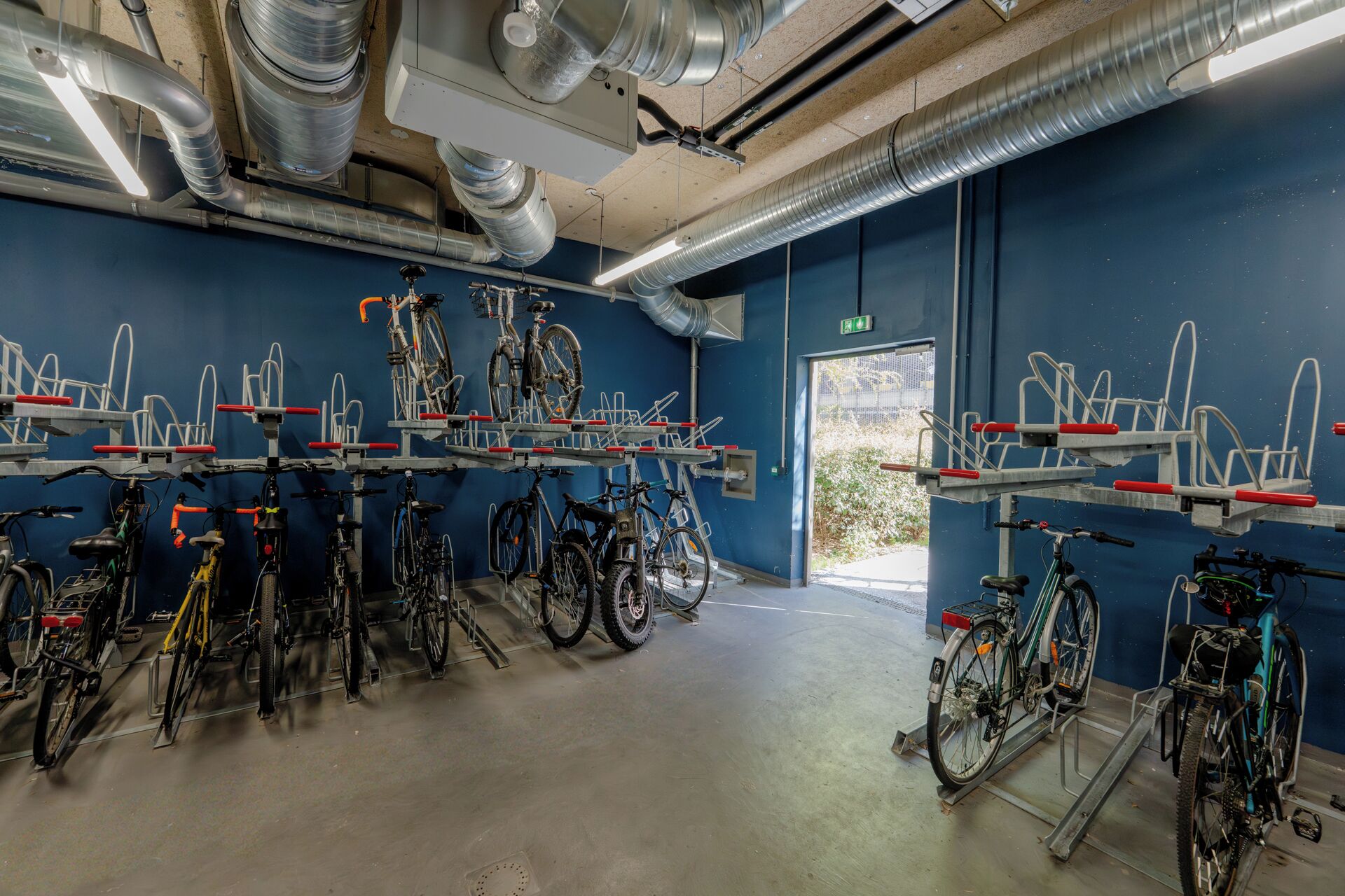 Een fietsverhuurstation met meerdere fietsen en fietsenrekken, een betonnen vloer en een blauwe muur.
