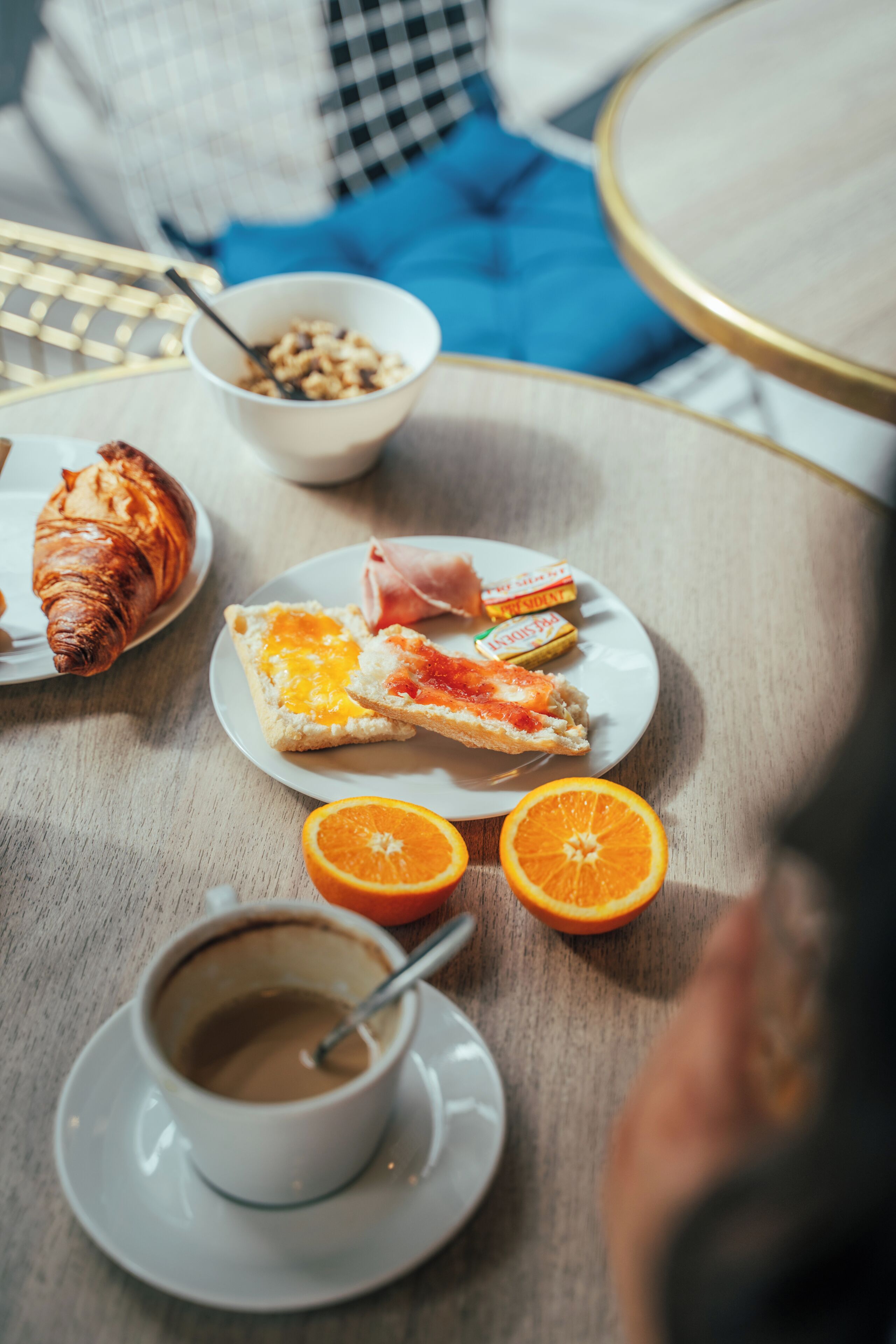 Una mesa de desayuno con cruasanes, gajos de naranja, un plato de comida y una taza de café.