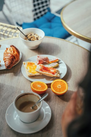 A breakfast table with croissants, orange slices, a plate of food, and a cup of coffee.