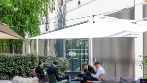 Ulkoterassi, jossa on pöytiä ja tuoleja, katettu alue sekä näkymä ikkunoilla varustettuun rakennukseen.