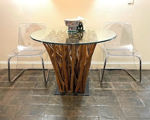 Une table ronde en verre, dotée d’un pied en bois original, et entourée de deux chaises en plastique transparent.