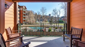 Un balcon avec des bancs en bois, une rambarde en métal et une vue sur une piscine et des immeubles.