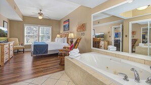 Une chambre d’hôtel dotée d’un grand lit, d’un coin salon avec un fauteuil, d’un bureau, d’une grande baignoire et d’un ventilateur de plafond.