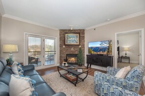 A living room with a fireplace, a television, a sofa, and a patterned armchair. - Baskins Creek 309 🏔️ Creekside Retreat | Pool, Hot Tub & Fireplace 🔥 (Gatlinburg)
