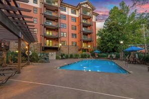 A multi-story building with a swimming pool, outdoor seating, and a stone facade. - Baskins Creek 312 🐻 Sleeps 6 | Pool Views, Hot Tub & Stone Fireplace 🔥 (Gatlinburg)