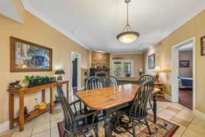 A dining area with a wooden table and chairs, a stone fireplace, and a hanging light fixture. - Baskins Creek 312 🐻 Sleeps 6 | Pool Views, Hot Tub & Stone Fireplace 🔥 (Gatlinburg)