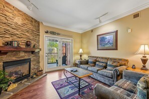 A living room with a stone fireplace, a sofa set, a coffee table, and a door leading outside. - Baskins Creek 312 🐻 Sleeps 6 | Pool Views, Hot Tub & Stone Fireplace 🔥 (Gatlinburg)