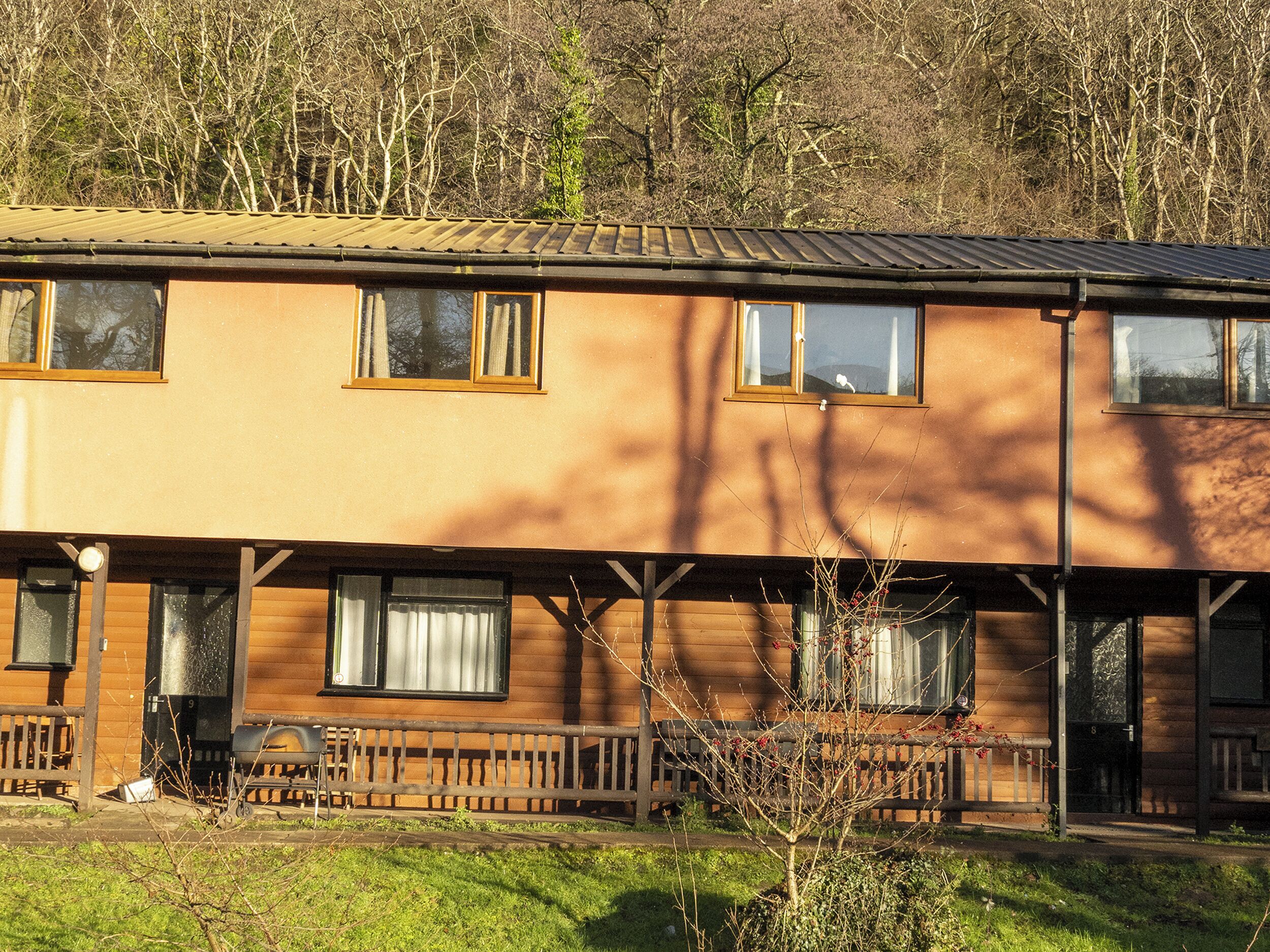 Ein zweistöckiges Holzhaus mit vielen Fenstern, einer Veranda mit Bänken und einer Rasenfläche davor.