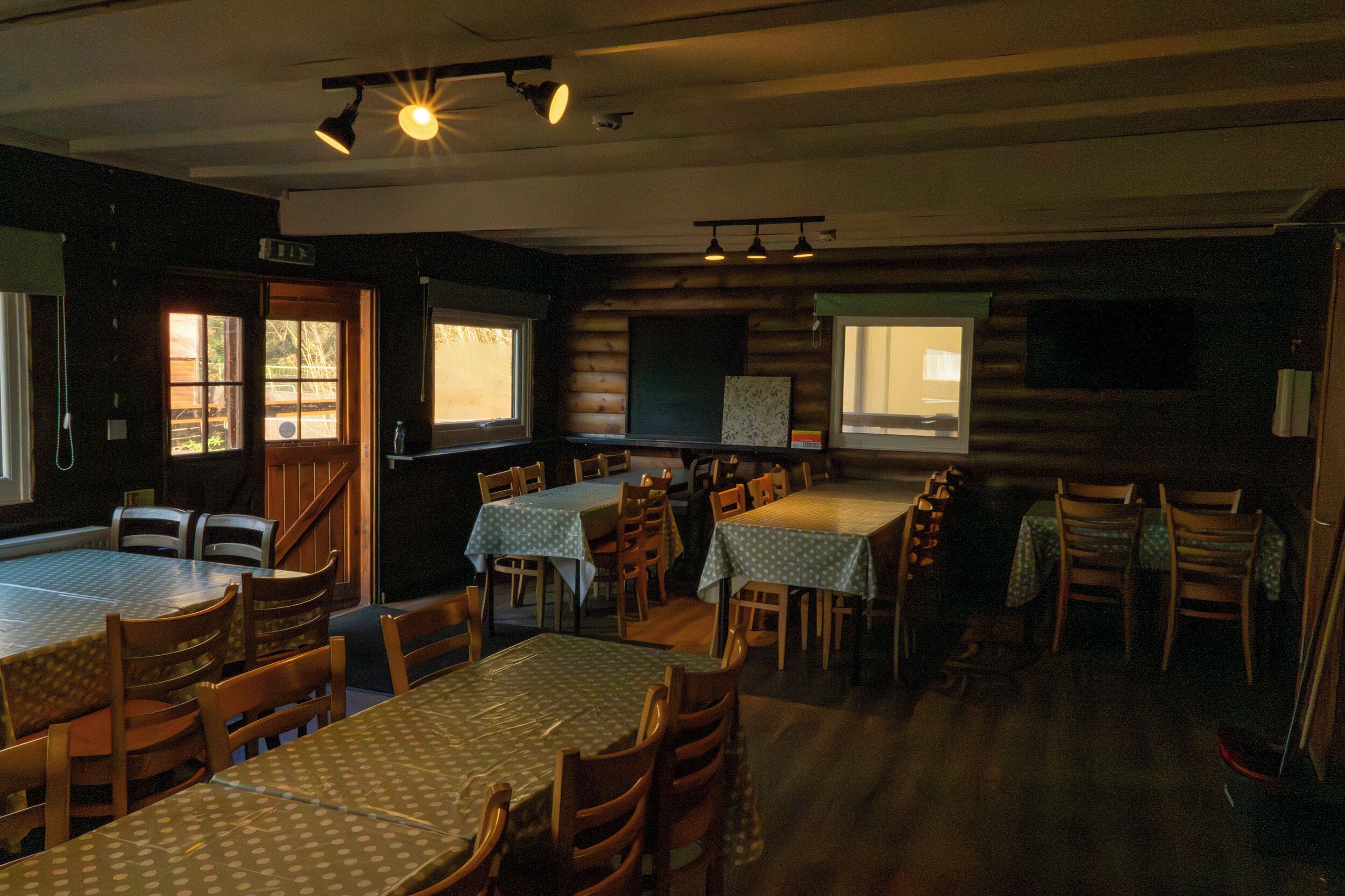 A dining area with tables and chairs, wooden walls, and windows.