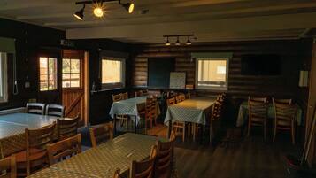 Un comedor con mesas y sillas, paredes de madera y ventanas.
