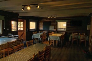 A dining area with tables and chairs, wooden walls, and windows. - Cabin No. 14 - Salt and Fern Cabins (Port Talbot)