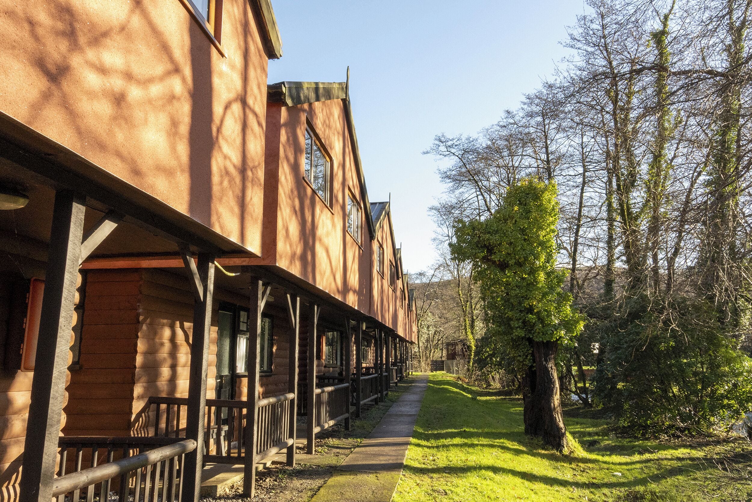 Un edificio in stile baita di legno con un portico coperto, un vialetto che conduce a una zona erbosa e alberi sullo sfondo.
