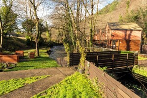 Una casa de madera rústica con un río al fondo, rodeada de vegetación y árboles.