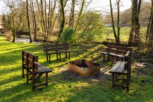 Un parque con bancos de madera y un pozo de fuego.