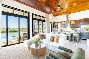 Ein modernes Wohnzimmer mit einem weißen Sofa, grünen Sesseln, einem Holztisch und Blick auf einen Pool und Außenbereich.