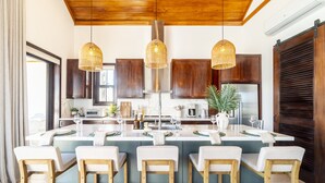 Een moderne keuken met een centraal eiland, houten barkrukken, hanglampen en donkerhouten kastjes.