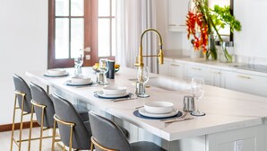 A modern kitchen with a central island, bar stools, a gold faucet, and a vase with flowers. - Abebi Oasis & Mistico Beach Club + Boat Shuttle (San Pedro)