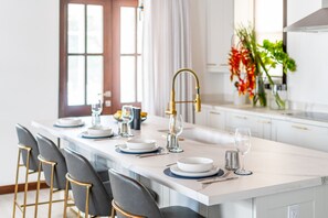A modern kitchen with a central island, bar stools, a gold faucet, and a vase with flowers. - Abebi Oasis & Mistico Beach Club + Boat Shuttle (San Pedro)
