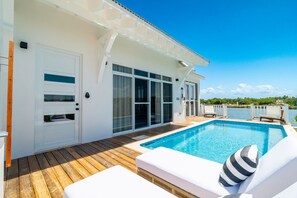 Ein Poolbereich mit Holzdeck, weißen Liegestühlen und einem klaren, blauen Pool.