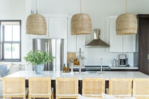 A kitchen with wicker pendant lights, a central island with chairs, a potted plant, and stainless steel appliances. - Cat`s Cradle & Mistico Beach Club + Boat Shuttle (San Pedro)