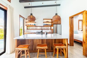 Een keuken met een centraal eiland, houten stoelen, hangende hanglampen en uitzicht op de omgeving.