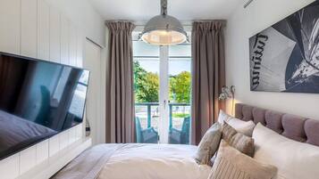 A bedroom with a bed, a TV, a ceiling light, a window with curtains, and a wall-mounted artwork.