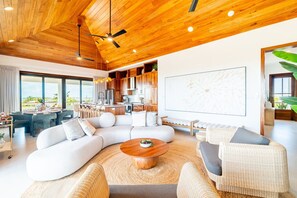 A modern living room with a large sectional sofa, a round coffee table, and a dining area with a view. - BelaDia at Mahogany Bay - Luxurious 10 Bedroom Compound (San Pedro)