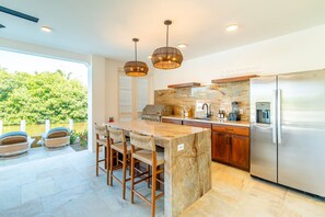 A modern kitchen with a marble countertop, stainless steel appliances, and a view of greenery outside. - BelaDia at Mahogany Bay - Luxurious 10 Bedroom Compound (San Pedro)
