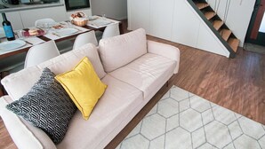 A modern living room with a sofa, a dining table with chairs, a kitchen area, and a staircase. - Travessa Apartments 3 Bedrooms By PontaNegraAzores (Praia da Vitória)