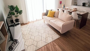 A modern living room with a sofa, a dining table, a kitchen area, and a large window with curtains. - Travessa Apartments 3 Bedrooms By PontaNegraAzores (Praia da Vitória)