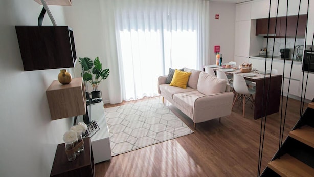 A modern living room with a sofa, a coffee table, a TV mounted on the wall, a dining area with a table and chairs, and a kitchen area with cabinets and appliances. - Travessa Apartments 3 Bedrooms By PontaNegraAzores (Praia da Vitória)